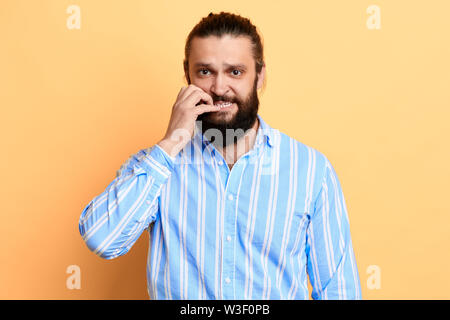nervous young man with worried expression biting his nails. close up portrait. isolated yellow background. studio shot. Stock Photo