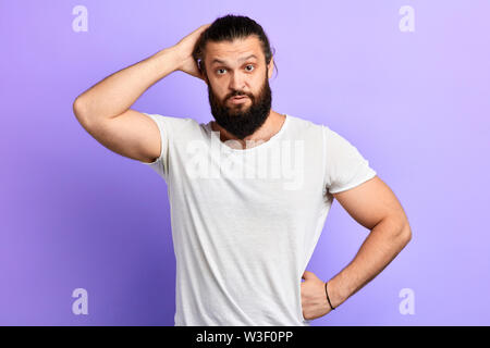 puzzled handsome man scratching his head in perplexity isolated over blue background. close up portrait. let me think difficult question . wait a minu Stock Photo
