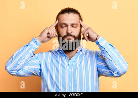 handsome guy with closed eyes holds fingers on temples, trying to remember something, massaging his head . isolated on a yellow background.close up po Stock Photo