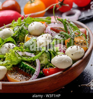 Vegetable salad with mocarella cheese, lettuce, cherry tomatoes, radish, cucumber, onion and basil in clay dish Stock Photo