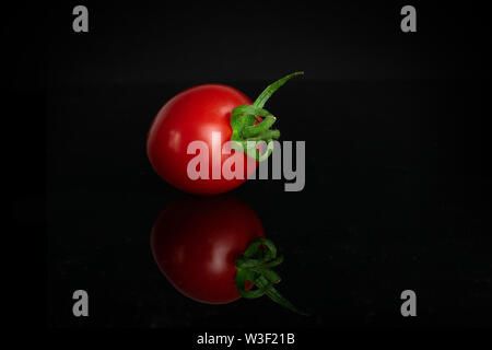 One whole fresh red tomato cherry isolated on black glass Stock Photo