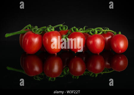Lot of whole fresh red tomato cherry in a row isolated on black glass Stock Photo