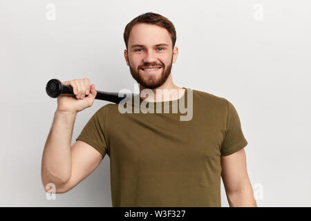 young cheerful happy man wearing a green T shirt, smiling and holding a baseball bat. close up photo. isolated white background. Stock Photo