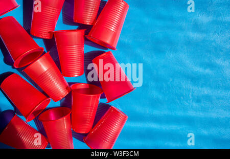 Disposable plastic tableware. Red glasses of red color on a blue background. The composition of the empty glasses. View from above. Copy space Stock Photo