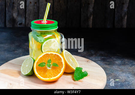 Can with cold and fresh lemonade. Lemon, orange, lime and mint on wooden background. Stock Photo