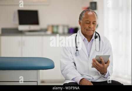 Contemplative male doctor using a digital tablet while sitting inside his office. Stock Photo