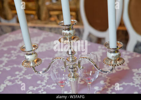 Three white candles on the table . three arms candle stick holder, two candelabra atop, on top of furniture, table against white wall in living room, Stock Photo
