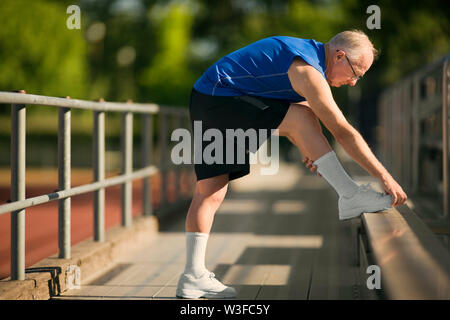 Senior man warming up with stretches on bleachers. Stock Photo