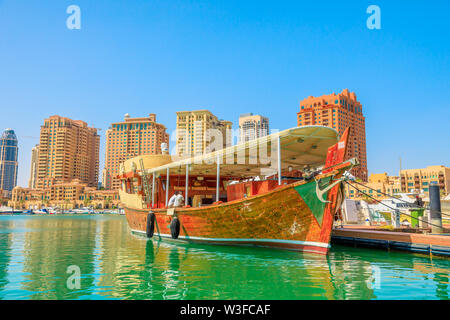 Doha, Qatar - February 18, 2019: traditional wooden boats docked in Porto Arabia at the Pearl-Qatar with residential buildings on background. Persian Stock Photo