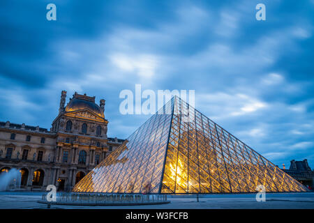 Paris, France - September 30, 2018: Iconic glass pyramid of Louvre museum with blurry motion of blue cloudy sky at sunset.