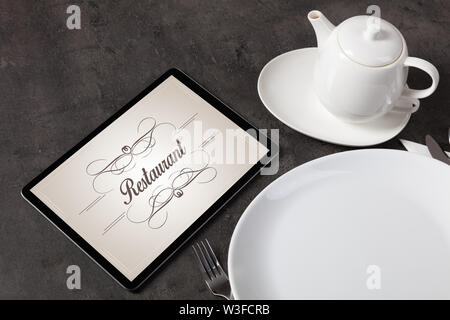Tablet with stylish restaurant logo and laid table Stock Photo