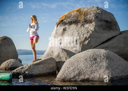 Active young woman practicing yoga on large rocks near the sea. Stock Photo