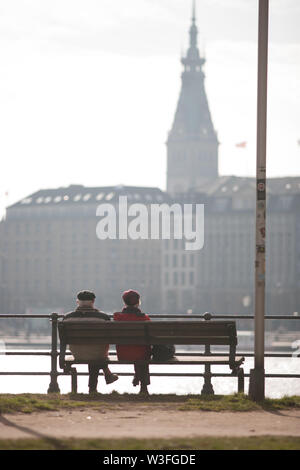 two old people sitting in front of a lake and houses behind the lake Stock Photo