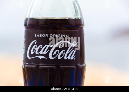 EL MEDANO, SPAIN - JULY 10 2019: Coca-Cola company logo on glass bottle with Coke with sea in background on July 10, 2019 in El Medano, Spain. Stock Photo