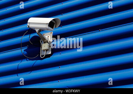 Security camera mounted on blue wall of corrugated sheet. Stock Photo