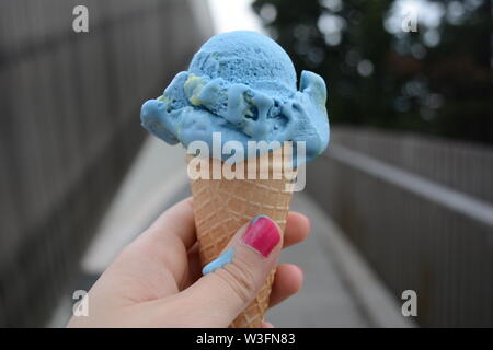 Photograph of a blue ice cream in a cone, held by a hand with pink fingernails Stock Photo