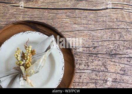 place setting on rsutic wood background with wood charger, cream colored plate with brown mottled edge and linen napkin with yellow berries napkin rin Stock Photo