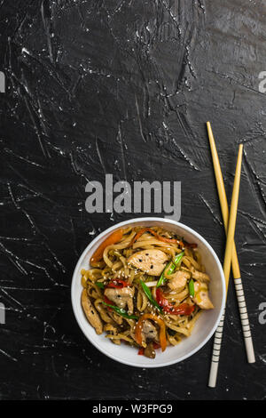 Chinese noodles in a Cup with chicken and vegetables with sticks. Wok food from the restaurant on a dark background from a top view. Stock Photo