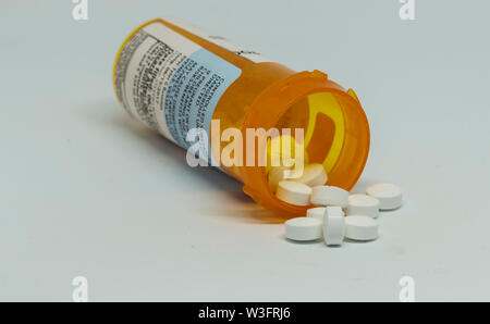 Pill bottle on its side with controlled substance pills falling out of the bottle with a white background. Stock Photo