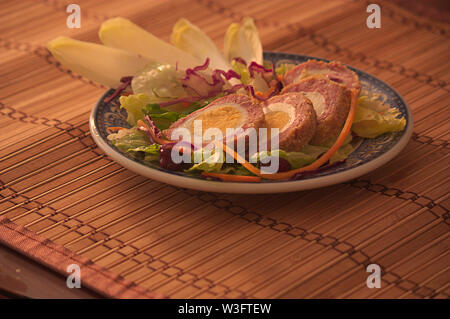 Plate with a serving of Scottish eggs accompanied with some vegetables with side light cooking. Dark food Stock Photo