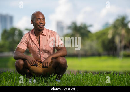 Handsome man looking off camera and smiling. Posing in a squat in the park with blurry background Stock Photo