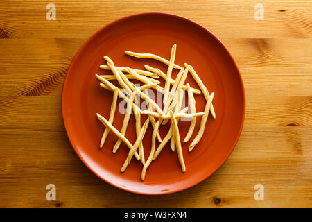 Raw strozzapreti pasta in a brown dish over a wooden background Stock Photo