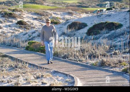 Elderly man walking hiking on boardwalk pathway through coastal dunes to relax at Asilomar Conference Center, Pacific Grove, California, USA Stock Photo