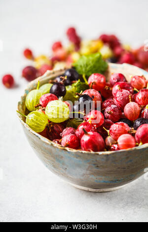 Red, green and black gooseberries in a bowl on a gray background. Stock Photo