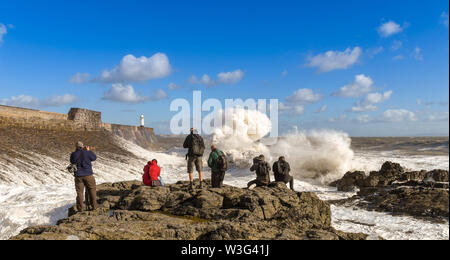 PORTHCAWL, EALES - OCTOBER 2018: Group of people on rocks taking pictures of large waves on the incoming tide. Stock Photo