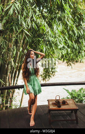 Beautiful young curly authentic woman in green dress is drinking healthy tea outdoor with nature background. Relax time concept. Stock Photo