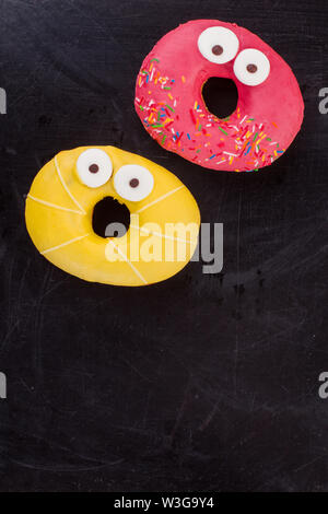 Funny donuts on black background, top view. Stock Photo