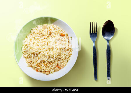 Noodles on the bowl with spoon and fork on green background Stock Photo