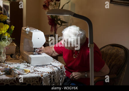 An elderly woman threads the needle on her Singer sewing machine in her home in Warren, Indiana, USA. Stock Photo
