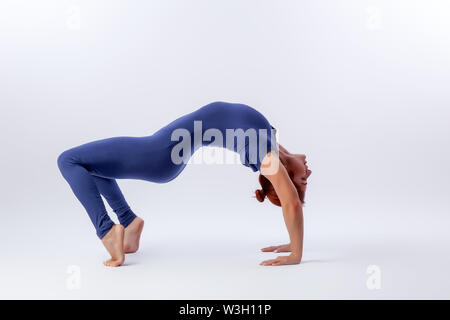 Beautiful slim woman in sports overalls  doing yoga, standing in an asana balancing pose - bridge outside of an overt bow on white  isolated backgroun Stock Photo