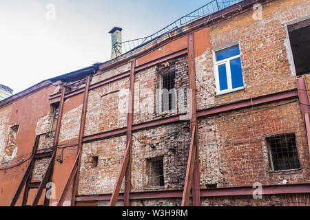 Brick wall of an old house in disrepair. To avoid collapse, the wall is reinforced with a metal structure.Site about building, architecture, hystory. Stock Photo