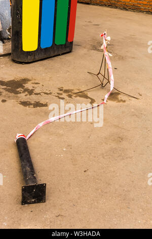 Red and white tape, prohibiting the passage, lying on the pavement. The black pillar is tumbled down. Stock Photo