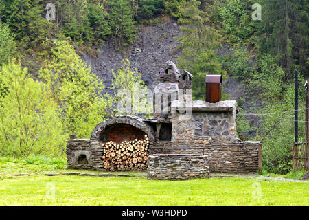 Old stone oven with wood, spit for meat and a smokehouse for cooking on the street in the Carpathians. Stock Photo