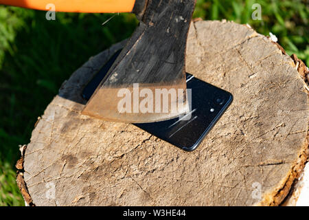 Ax cuts the phone. Destroy innovation. Vandalism act. Smartphone on the stump. Smartphone near the ax. The ax in the stump Stock Photo