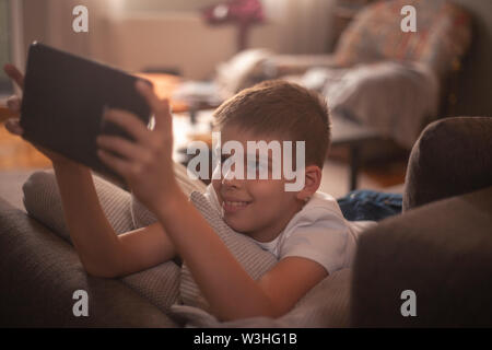 one happy and smiling boy using tablet, sitting in couch, relaxing in his home. Stock Photo