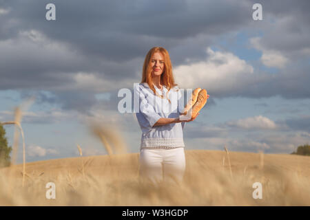 Redhead woman with two french loaves in ripe wheat field Stock Photo