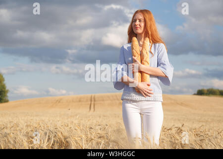 Redhead woman with two french loaves in ripe wheat field Stock Photo