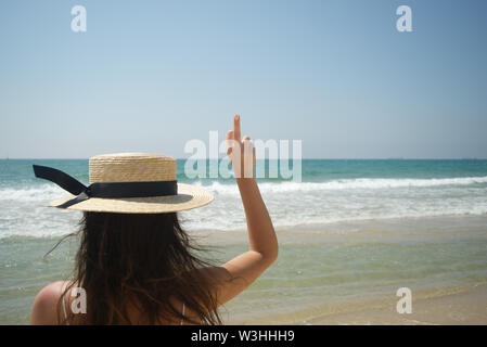 Young female sticking middle finger up, standing on the beach, outdoor shot Stock Photo
