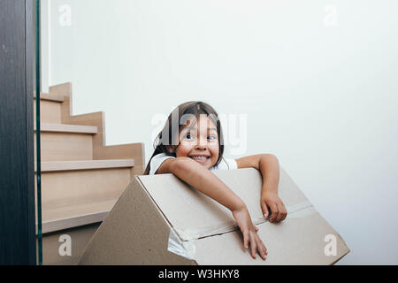 Cute little girl holding cardboard box and sitting on stairs Stock Photo