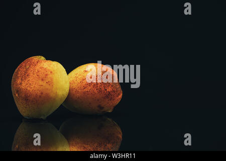 Beautiful two fresh apricots on a black glass table background. Stock Photo