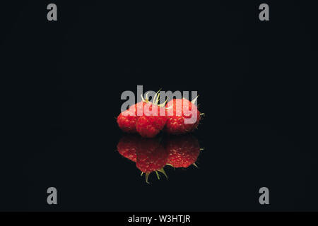 Beautiful three fresh raspberry on a black glass table dark background. Stock Photo