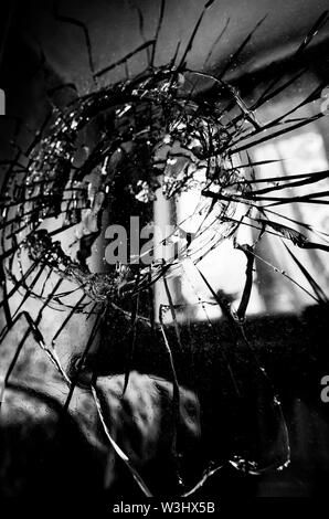 Broken glass with cracks and a hole stylized black and white film in the background of the blurred room closeup Stock Photo