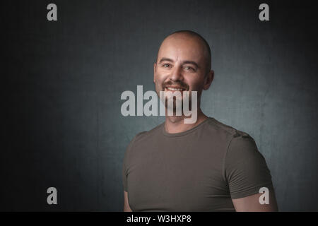 portrait of smiling caucasian man with t-shirt and dark background. Shot taken in the studio. Stock Photo