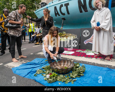 London, UK. 15th July, 2019. People bring water from across the country and pout it into a bowl. Extinction Rebellion begins another series of protests in five major cities against the criminal inaction by the government on climate and ecological collapse. The protesters brought a yacht named after Polly Higgins who fought for years for an Ecocide Law to the Royal Courts of Justice and continued her fight blocking the Strand all day with performances, discussions, speeches, music and ceremonies in front of the yacht. Credit: Peter Marshall/Alamy Live News Stock Photo