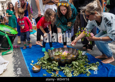 London, UK. 15th July 2019. People add flowers to water from across the country in a ceremony against ecocide. Extinction Rebellion begins another series of protests in five major cities against the criminal inaction by the government on climate and ecological collapse. The protesters brought a yacht named after Polly Higgins who fought for years for an Ecocide Law to the Royal Courts of Justice and continued her fight blocking the Strand all day with performances, discussions, speeches, music and ceremonies in front of the yacht. Peter Marshall/Alamy Live News Stock Photo