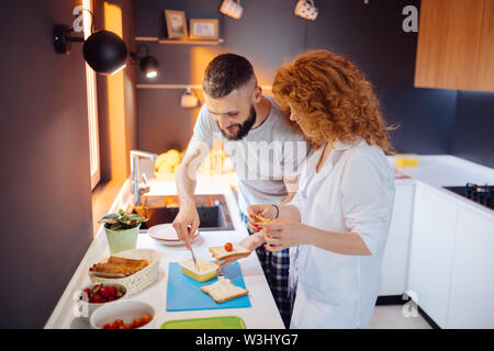 Involved in process. Nice joyful man spreading cheese on the bread while being involved in process of making sandwiches Stock Photo